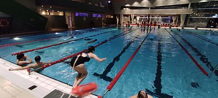 Eine Rettungsschwimmerin springt im Hallenbad vom Beckenrand ins Schwimmbecken. 