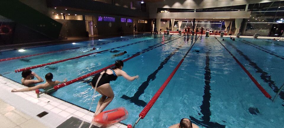 Eine Rettungsschwimmerin springt im Hallenbad vom Beckenrand ins Schwimmbecken. 