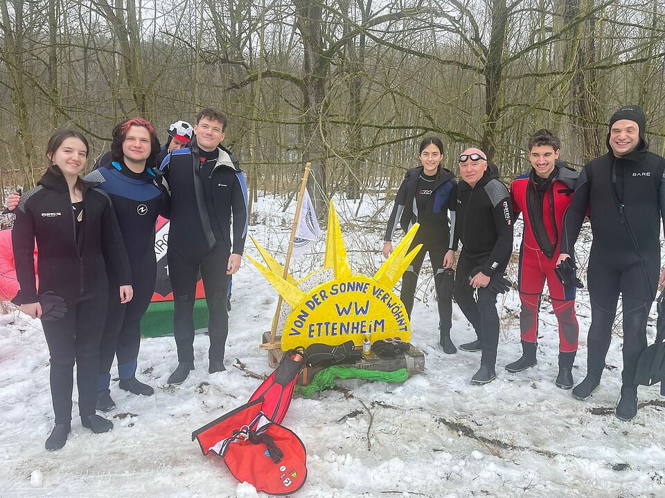 Rettungsschwimmer der Wasserwacht Ettenheim stehen beim Donauschwimmen in Neuburg in Neoprenanzügen um ein selbstgebautes Floss