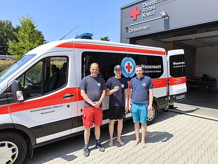 Drei Einsatzkräfte der Wasserwacht stehen vor einem Tauchwagen